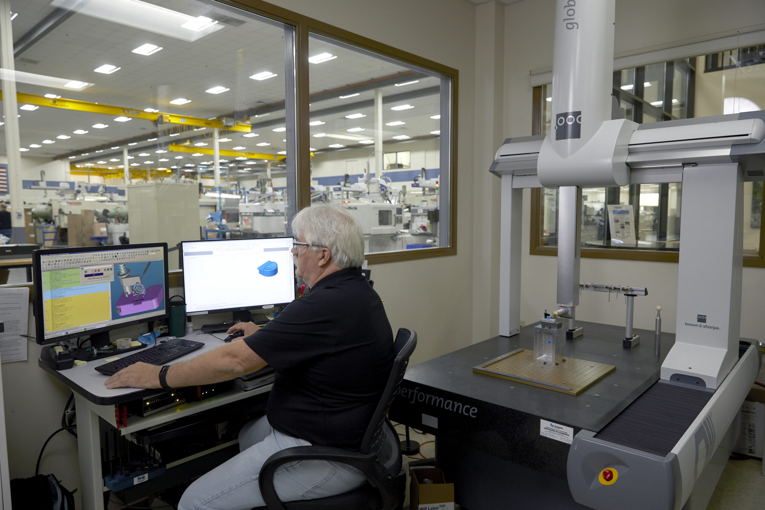 A Velosity employee works at a computer with machinery behind him